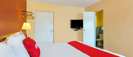 Ein Hotelzimmer mit Bett, Fernseher, einer Tür und einem durch eine offene Tür einsehbaren Badezimmer.