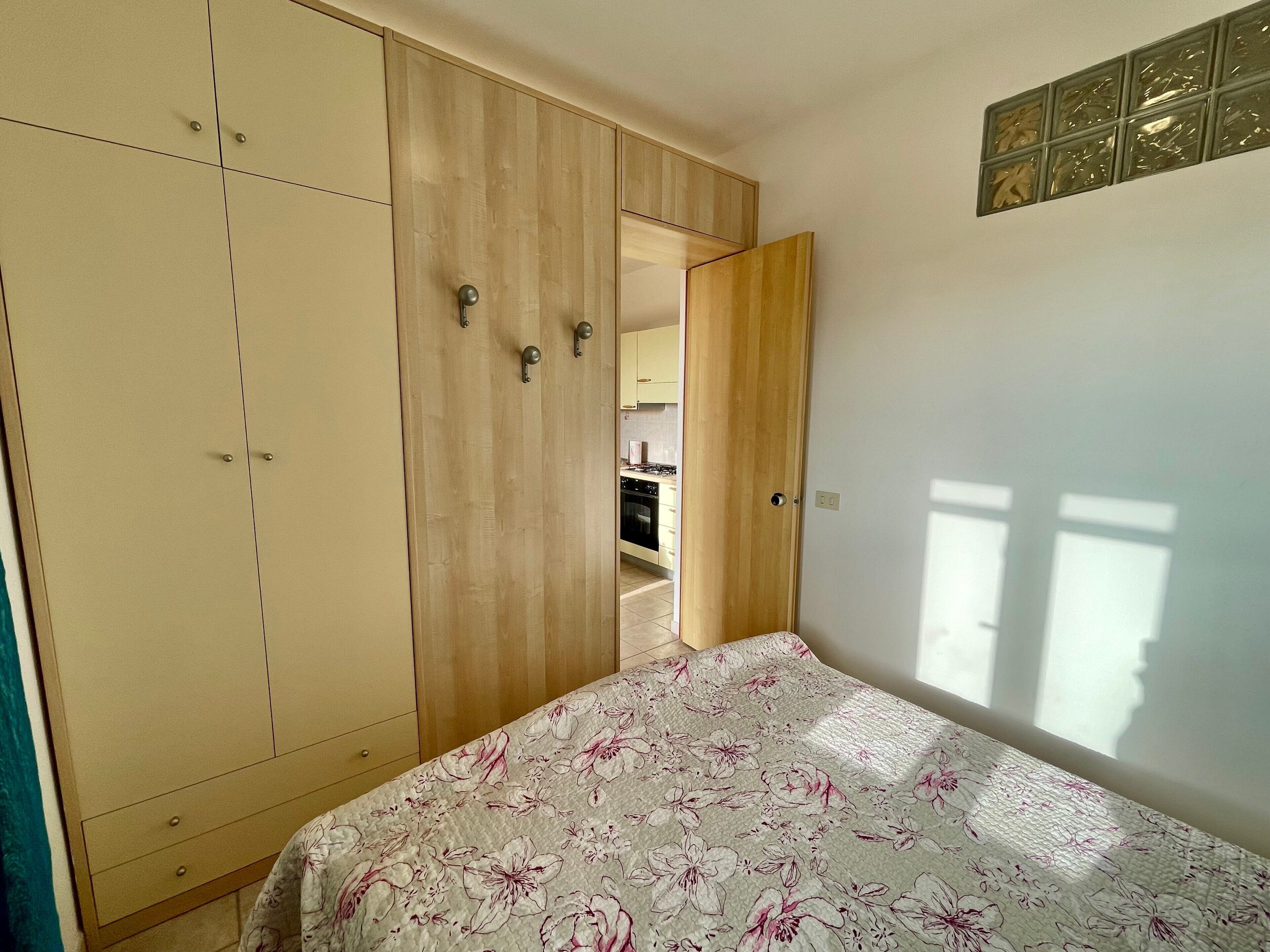 A bedroom with a bed, wardrobe, and a door leading to a kitchen.