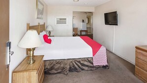 Ein Hotelzimmer mit einem Bett, Nachttischlampen, einem Fernseher, einer hölzernen Kommode und einer Tür.