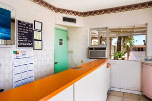 A reception area with a check-in counter, a wall-mounted AMTEX calendar, a private door, and a window with a view of the outside.