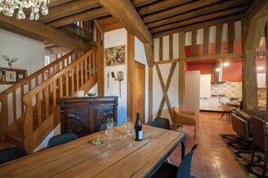Ein Essbereich mit einem Holztisch, Stühlen und einer Weinflasche. Eine Treppe mit hölzernen Geländern führt in einen anderen Raum.