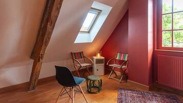 A room with a sloped ceiling, a skylight, two chairs, a small table, and a radiator.