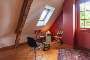 Ein Zimmer mit schrägen Wänden, einem Oberlicht, zwei Stühlen, einem kleinen Tisch und einer Heizung.