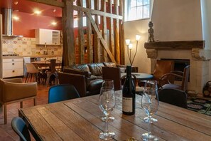 A dining area with a wooden table, wine glasses, and a bottle. There is a kitchen in the background with a red wall and a staircase. - La Ruelle des Chats House, Historic Center of Troyes (Troyes)