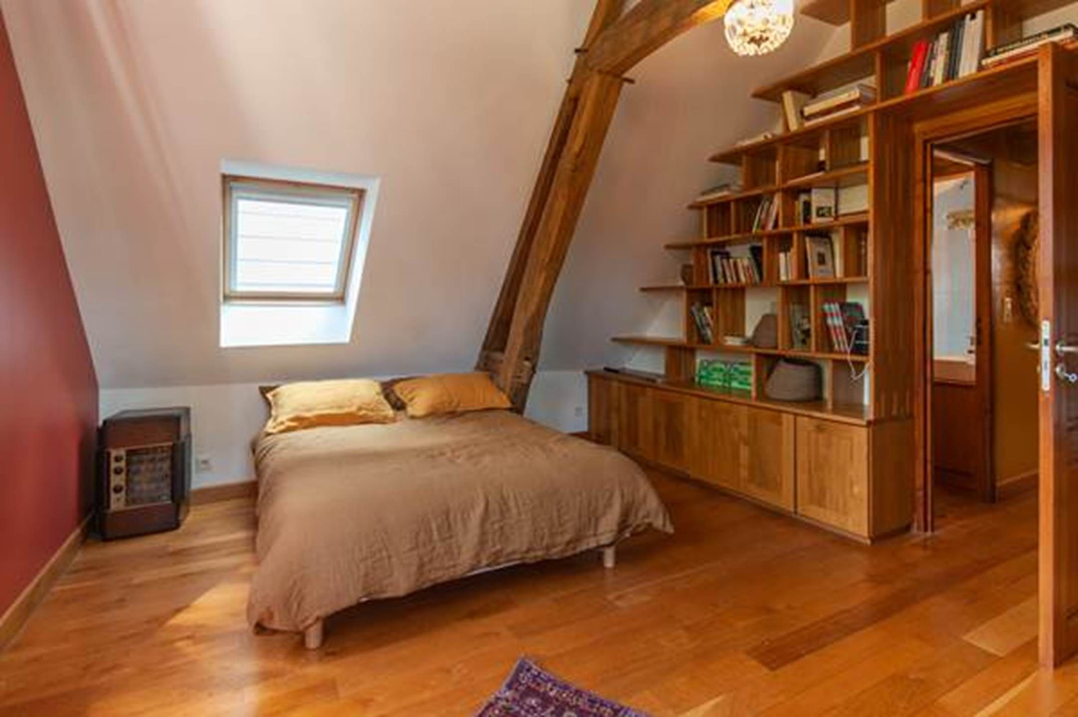 Une chambre avec un plafond en pente, un lit, une bibliothèque en bois et une fenêtre.
