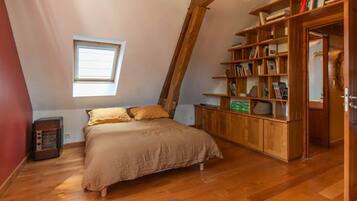 Une chambre avec un plafond en pente, un lit, une bibliothèque en bois et une fenêtre.