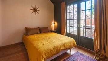 Une chambre avec un lit, une décoration en forme d’étoile sur le mur, une table de chevet avec une lampe, et une vue par une fenêtre avec des rideaux.