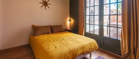 Un dormitorio con cama, decoración de estrella en la pared, mesita de noche con lámpara y vistas a través de una ventana con cortinas.
