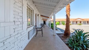 A covered walkway with white brick walls, benches, and a palm tree.