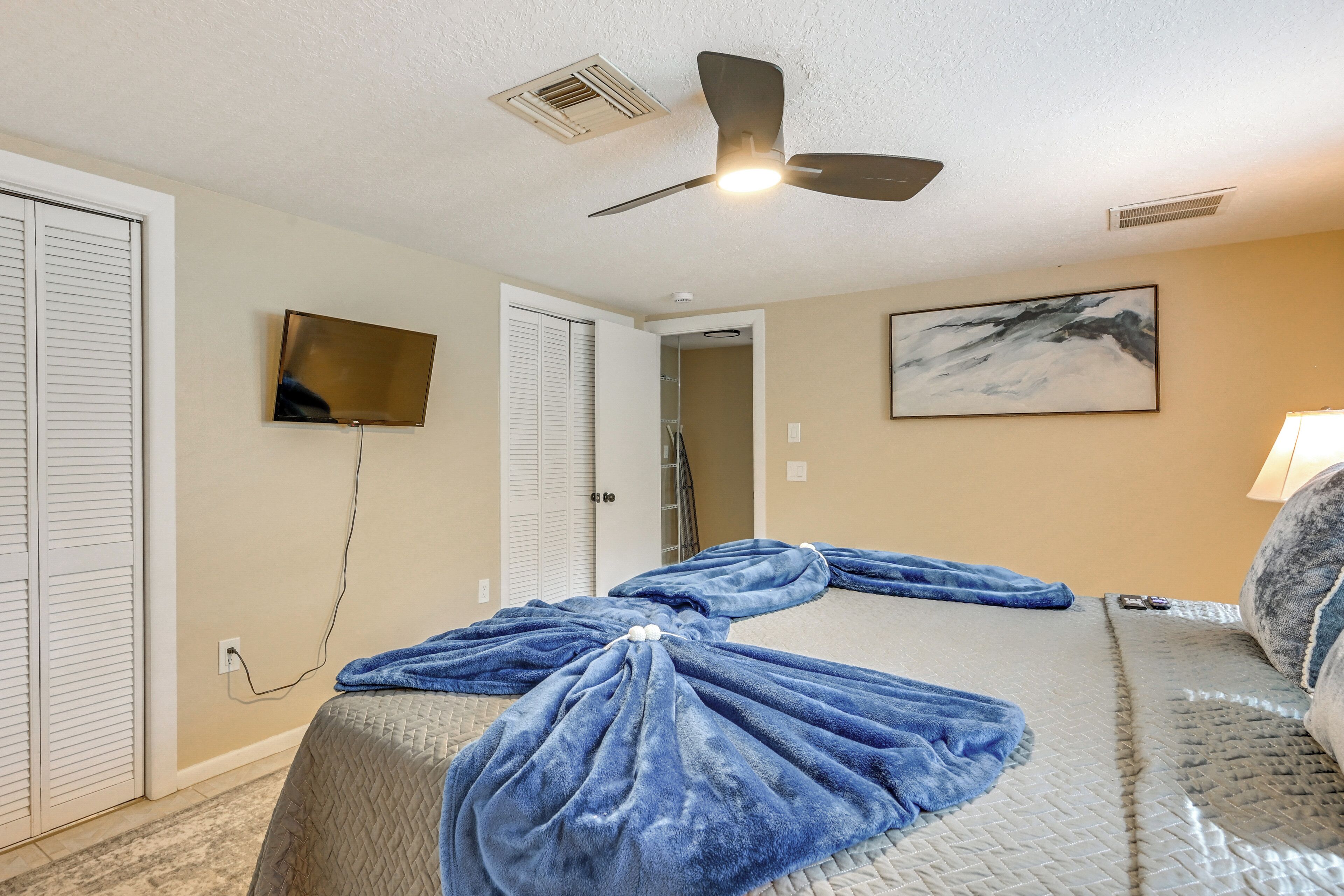 Habitación de hotel con cama, ventilador de techo, televisor, un cuadro y la puerta del baño.