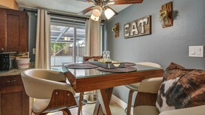 A dining area with a glass-top table, wooden chairs, a ceiling fan, and a kitchen in the background. - Private Pool! Port Richey Home Near Coast & Trails (Port Richey)
