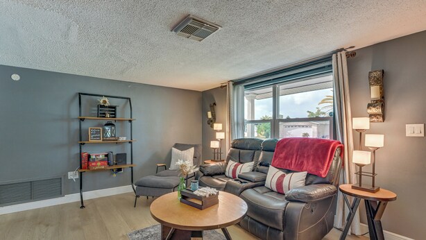 A modern living room with a leather sofa, a coffee table, a bookshelf, and a window with curtains. - Private Pool! Port Richey Home Near Coast & Trails (Port Richey)