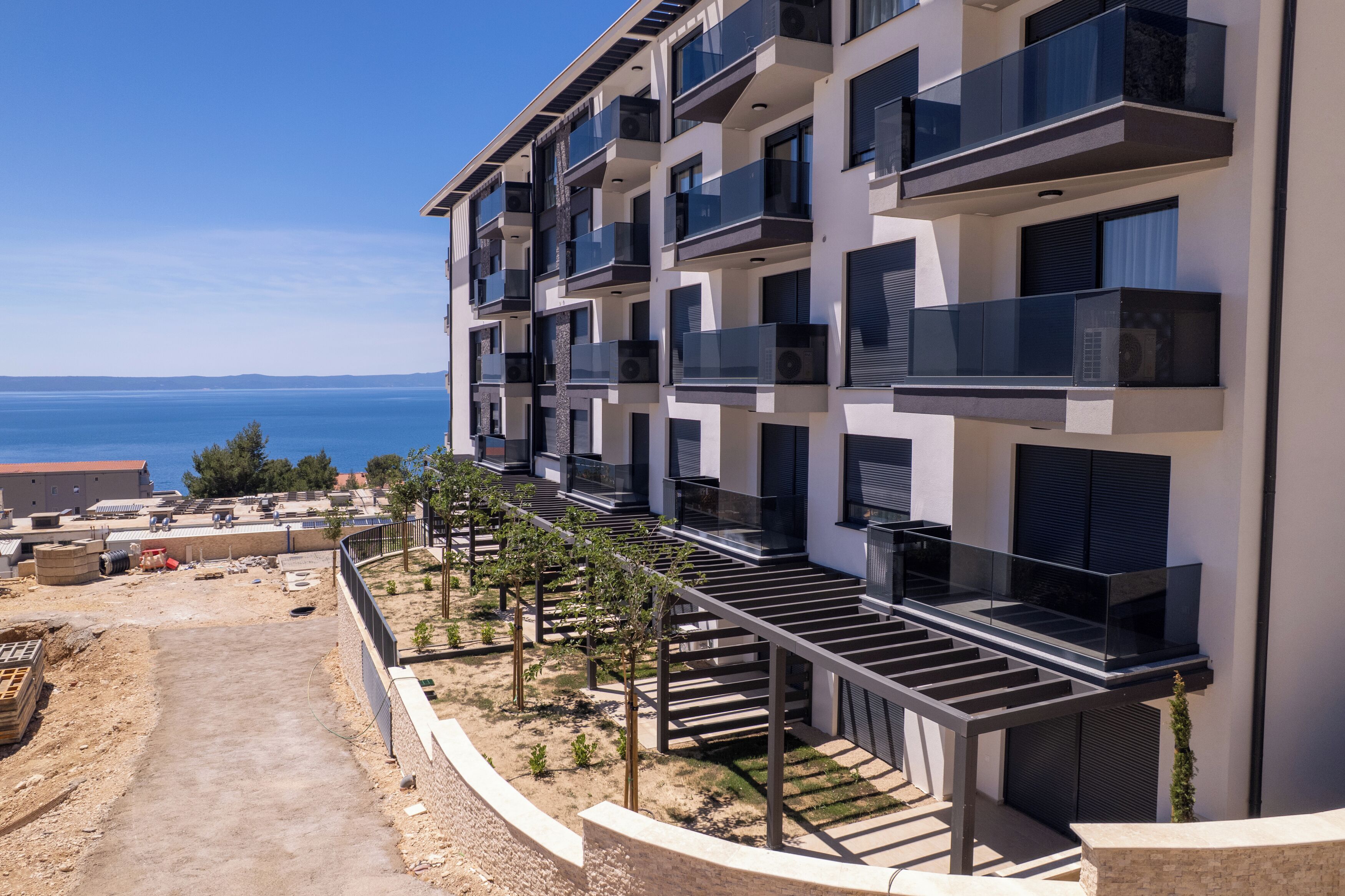 A multi-story residential building with balconies, a clear view of the sea, and a construction site nearby.