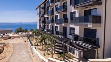 A multi-story residential building with balconies, a clear view of the sea, and a construction site nearby.