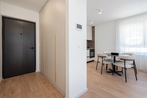 Ein modernes Wohnzimmer mit Essbereich, einer Küche im Hintergrund und einem großen Fenster mit durchsichtigen Vorhängen.