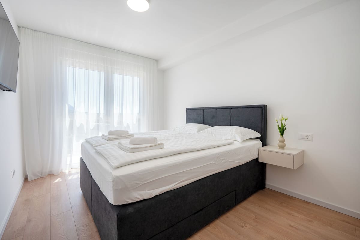 Une chambre à coucher moderne avec un lit, une table de chevet et une fenêtre avec des rideaux.