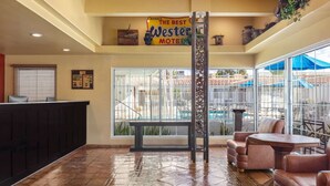 A reception area with a sign reading 'The Best Western Motel,' a reception desk, seating area with chairs and tables, and a view of a pool through large windows.