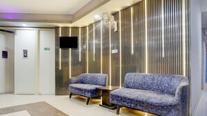 A lobby with a reception desk, two sofas, a flat-screen TV, and a patterned wall. - Saver Double Patparganj Near Max (New Delhi)
