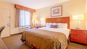Una habitación de hotel con una cama grande, dos lámparas de noche, un cabecero, un cuadro enmarcado en la pared y una ventana con cortinas.