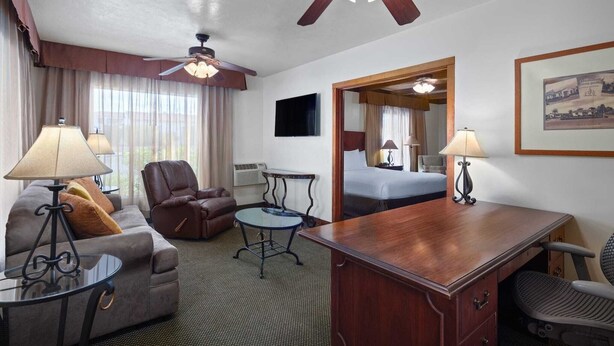 Habitación de hotel con sofá, sillón, escritorio y ventilador de techo.