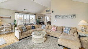 Un salon avec un canapé d’angle, une table basse ronde et un panneau décoratif représentant une maison de plage accroché au mur.