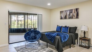 Un dormitorio con cama, una silla, una mesita de noche, una lámpara y un cuadro en la pared.