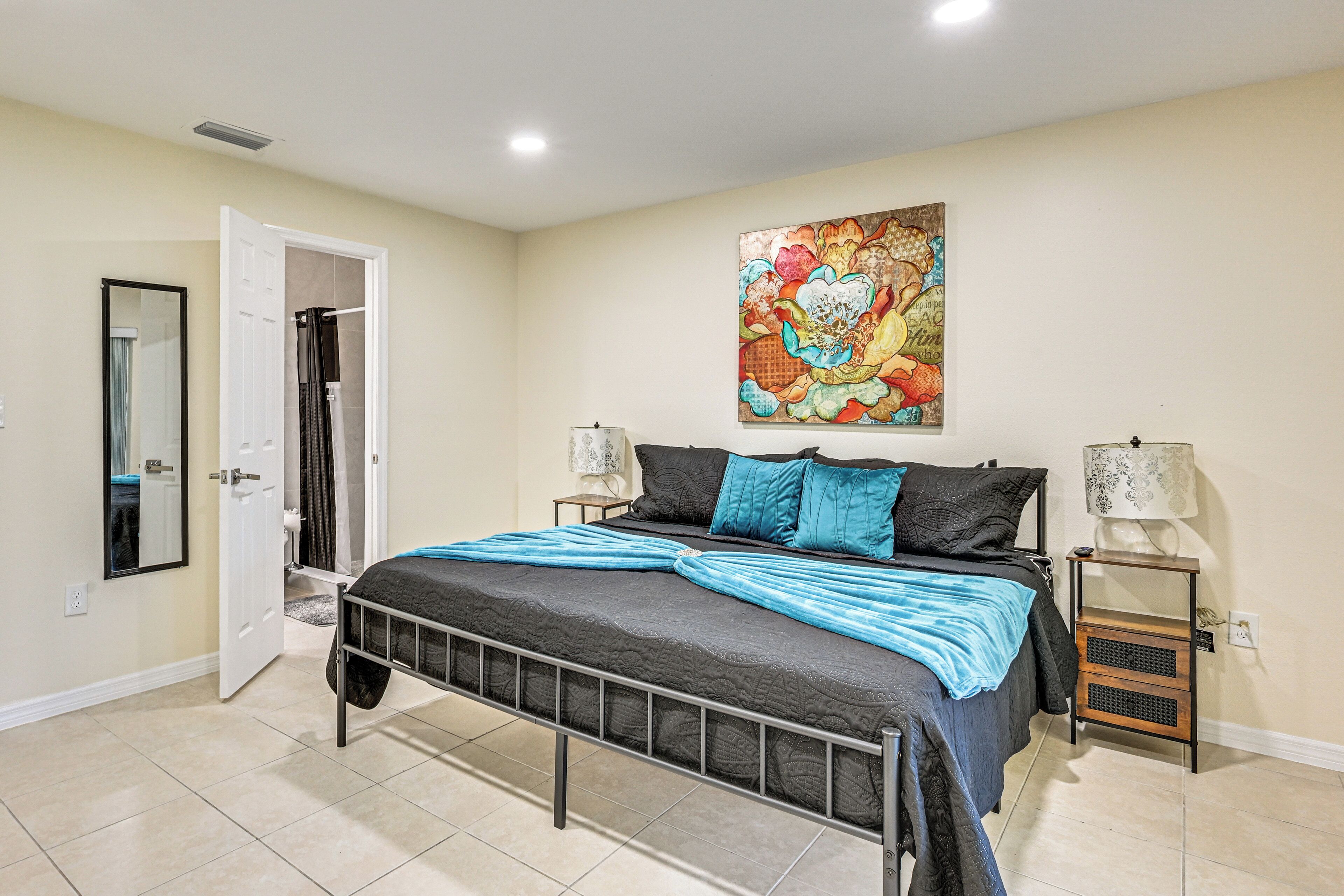 A bedroom with a bed, a door, a wall-mounted artwork, and a bedside table with a lamp.