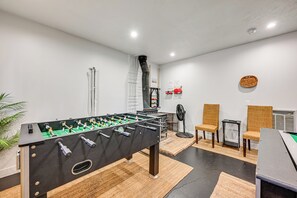 Ein Zimmer mit einem Kicker, zwei Korbstühlen, einem Ventilator und einem kleinen Tisch mit einer Plakette.