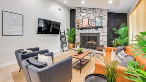 Uma sala de estar moderna com lareira de pedra, assentos confortáveis e uma televisão de tela plana na parede.