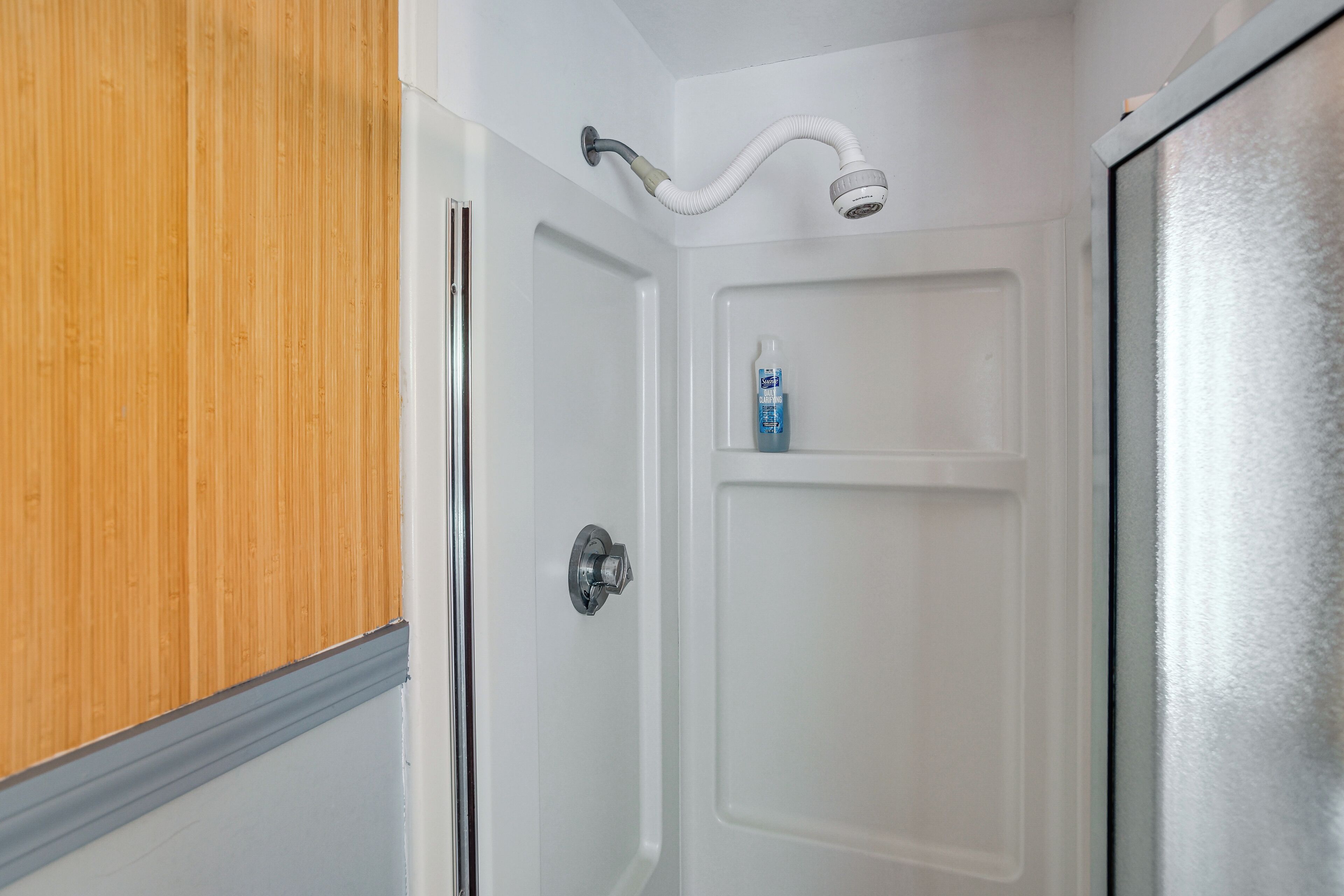 A bathroom with a shower, a toilet, and a shelf with a bottle.
