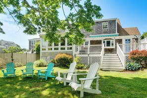 Ein Haus mit einer Terrasse, einer Treppe und drei Adirondack-Stühlen im Garten.