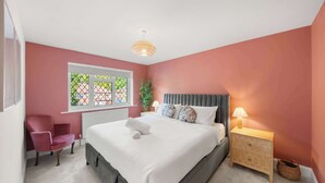 Un dormitorio con cama, una silla, una mesita de noche, una lámpara y una ventana.
