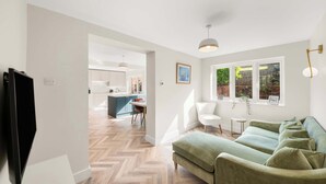 Una sala de estar moderna con un sofá verde, piso de espiga y una cocina al fondo.
