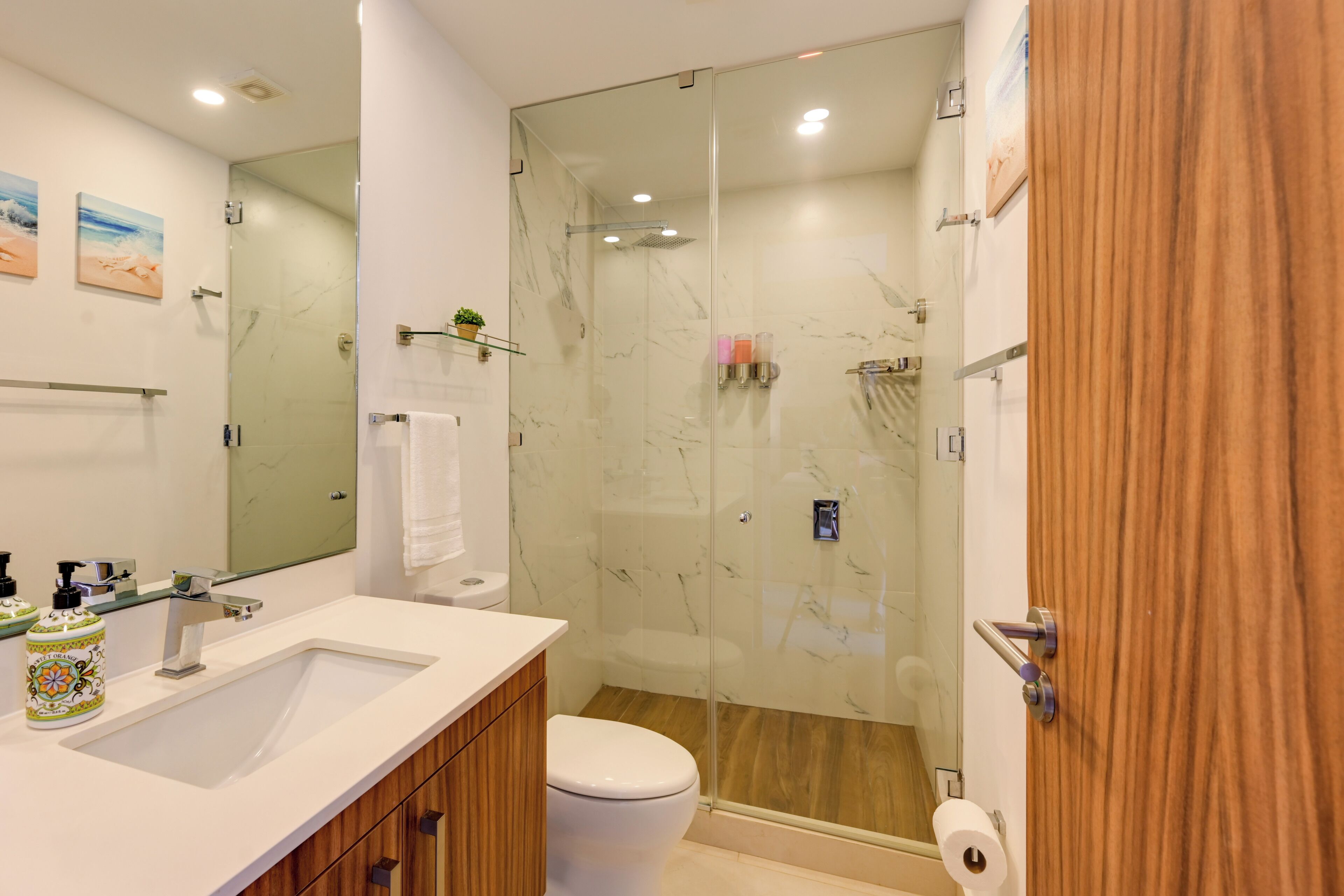 Un baño moderno con ducha de vidrio, lavamanos blanco y tocador de madera.