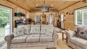 Ein Interieur einer Hütte mit Holzbalkendecke, einer Couch mit Tiermotiv, einem Esstisch und einer Küchenzeile.
