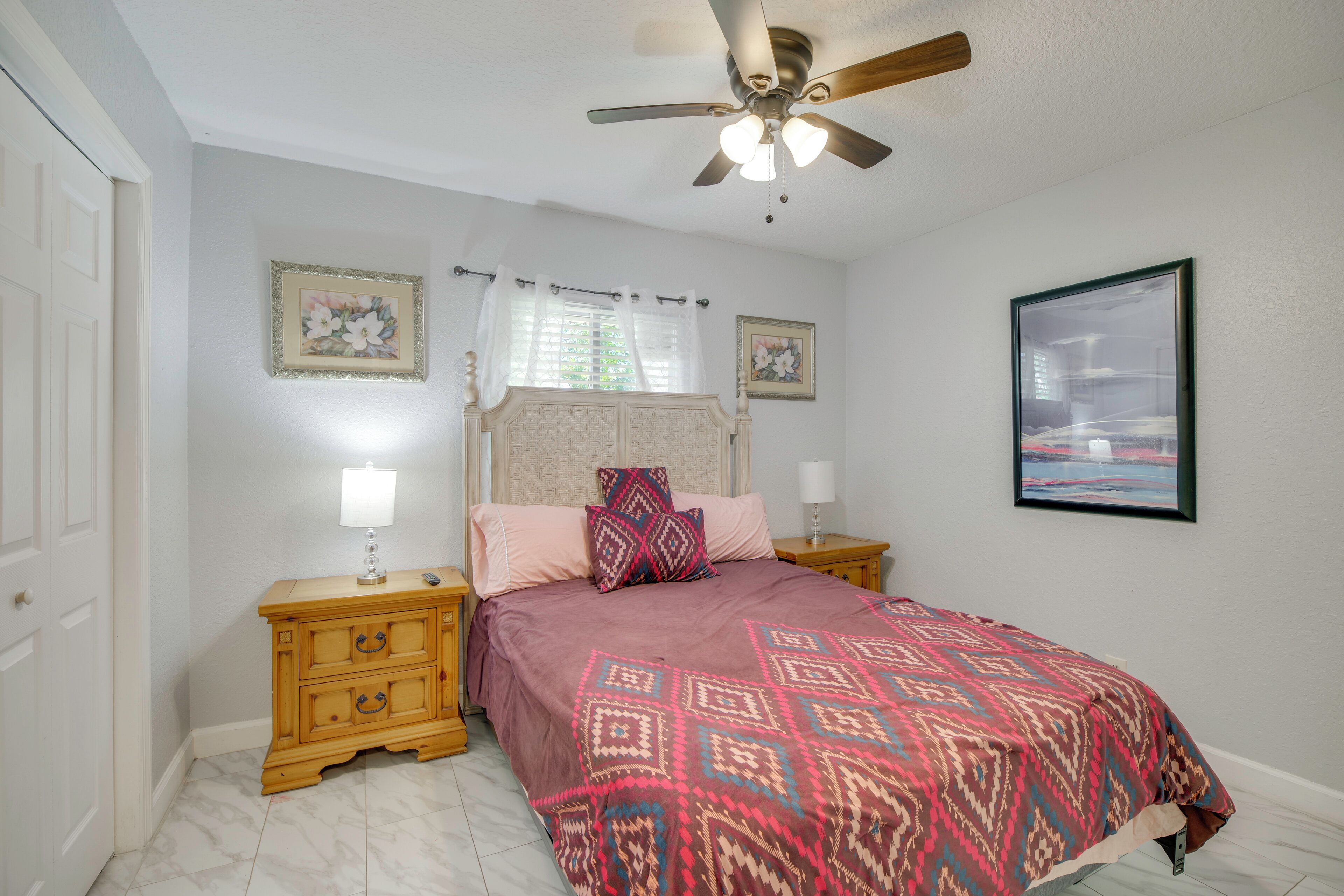 A bedroom with a bed, nightstands, a ceiling fan, and framed artwork on the walls.