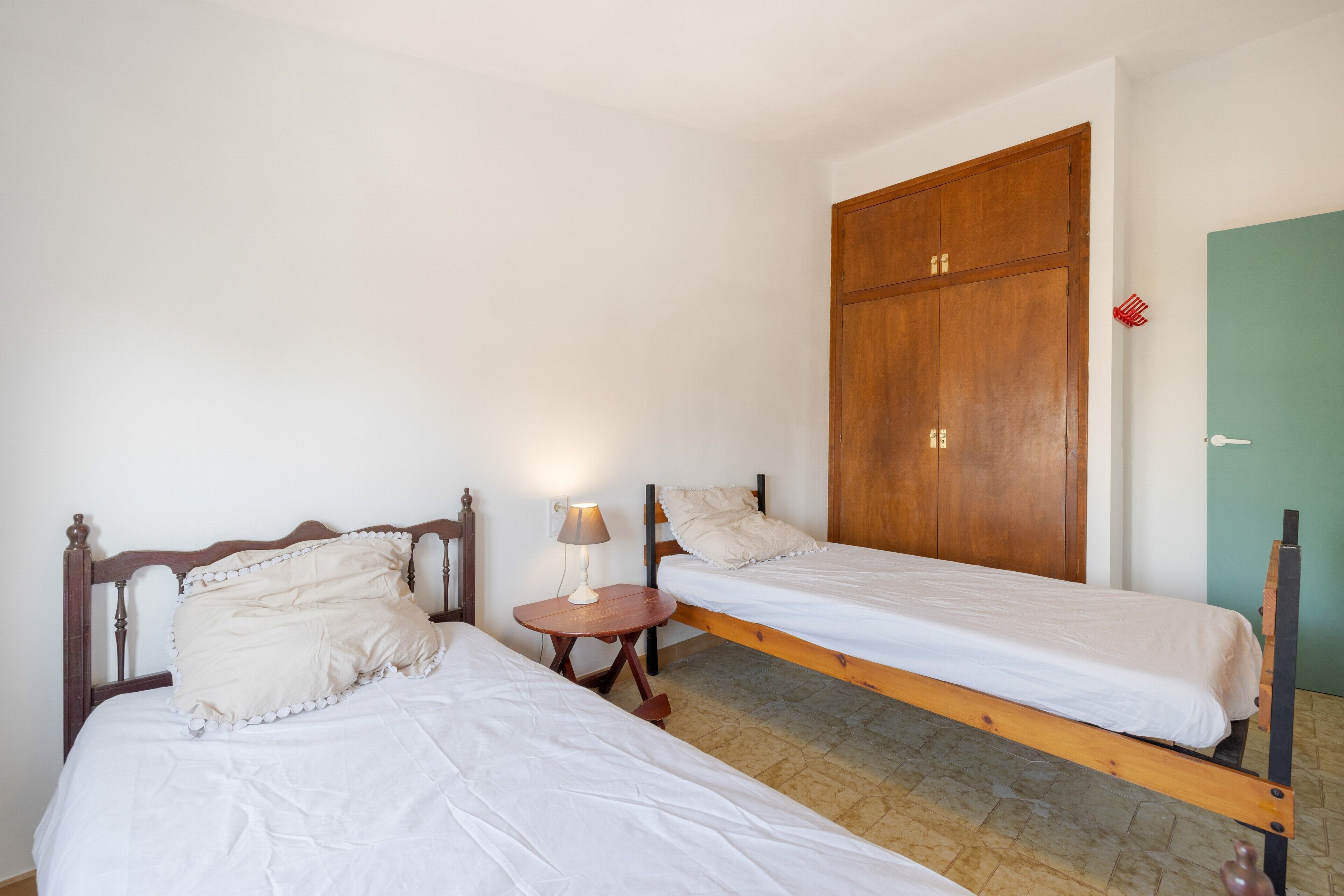 Una habitación con dos camas de madera, una mesita con una lámpara y un armario de madera grande.