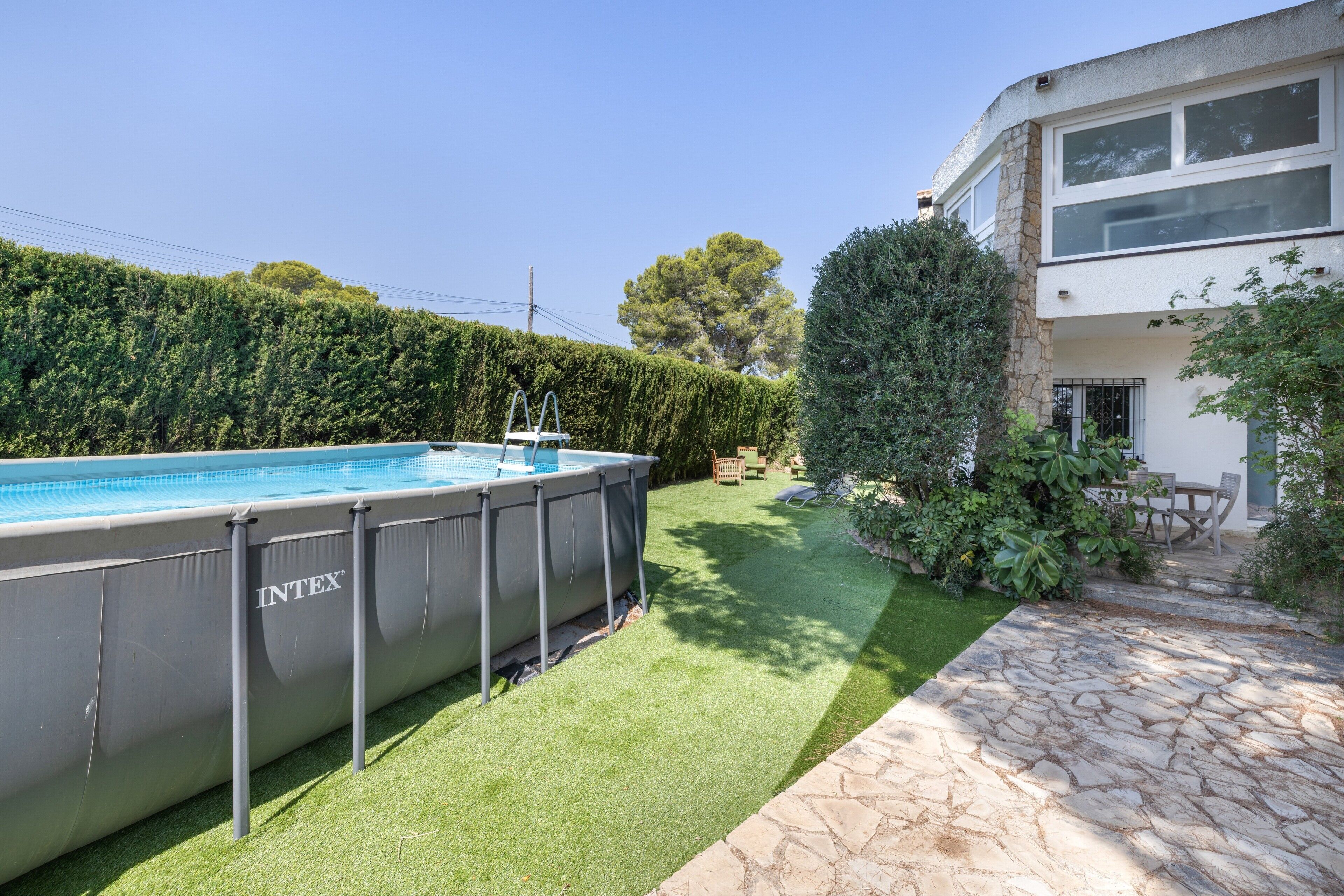 A swimming pool, stone patio, and a modern house with a stone facade.