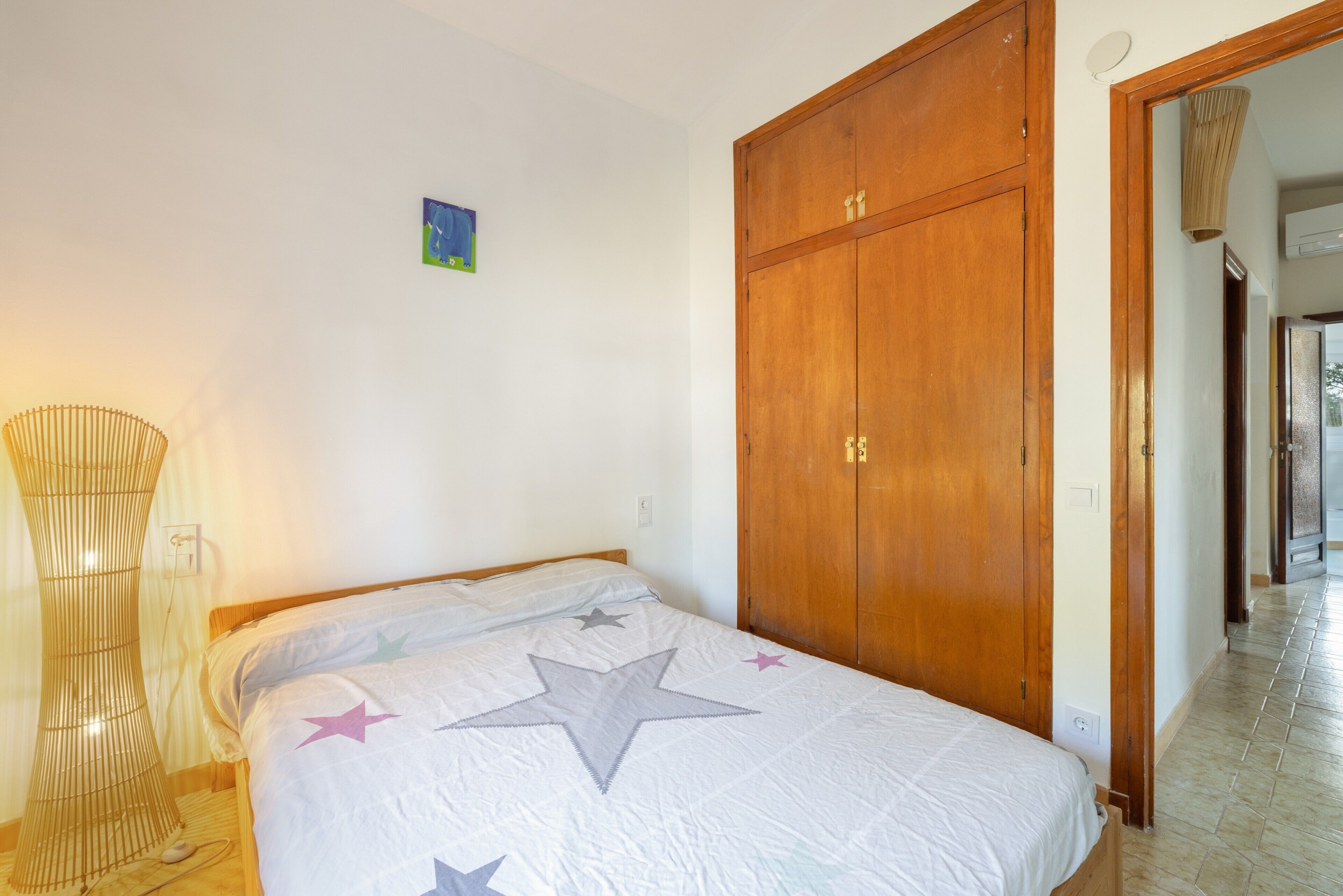 A bedroom with a bed, a wooden wardrobe, and a lamp.