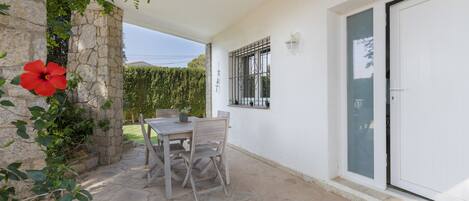 A patio with a table and chairs, a stone wall, a red flower, and a white door.