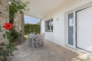 Eine Terrasse mit Tisch und Stühlen, eine Steinmauer, eine rote Blume und eine weiße Tür.