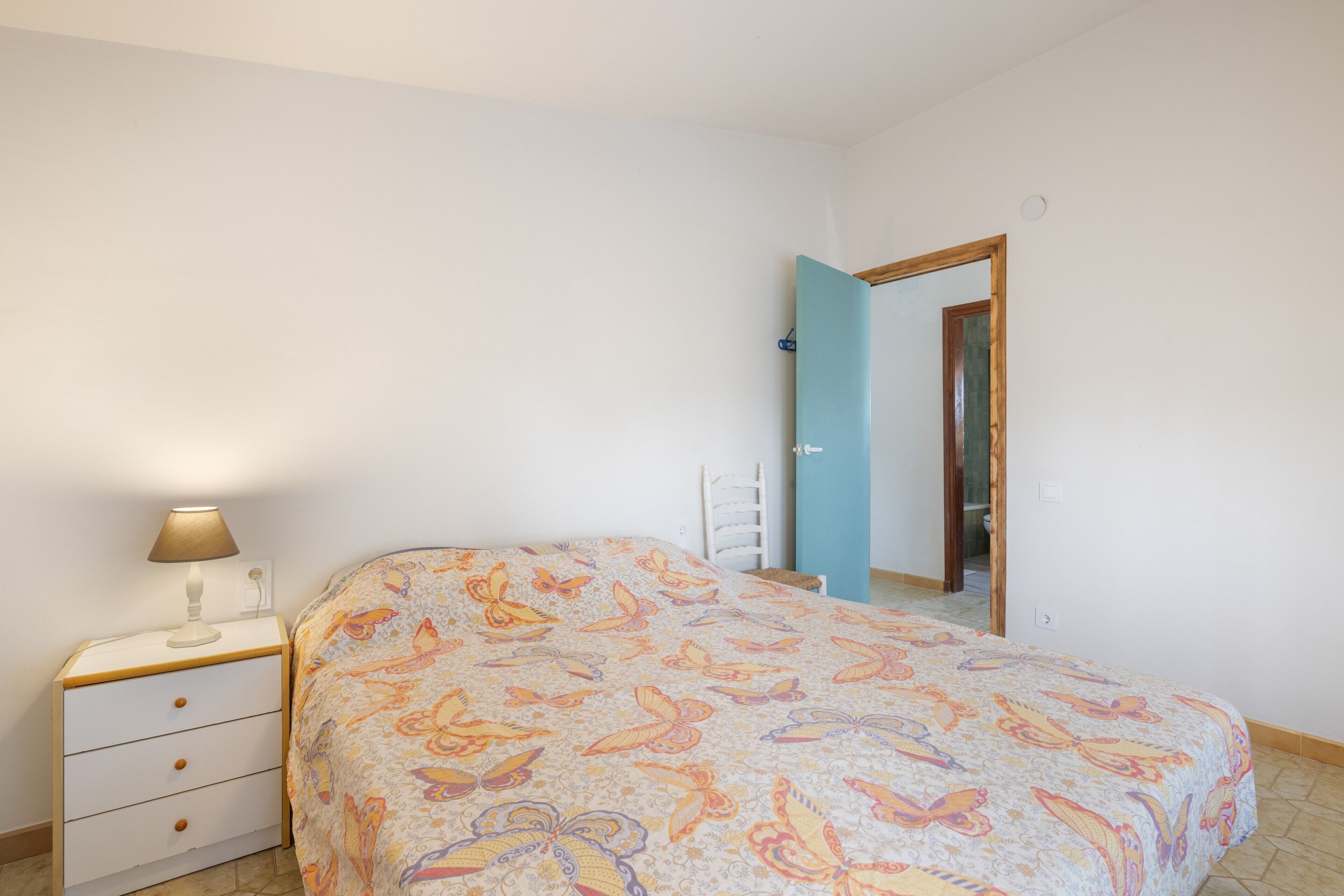 A bedroom with a bed, a nightstand, a lamp, and a door leading to another room.