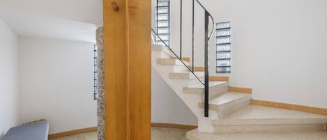 Una escalera con barandilla de madera y pasamanos metálico, que conduce a un rellano con ventana.
