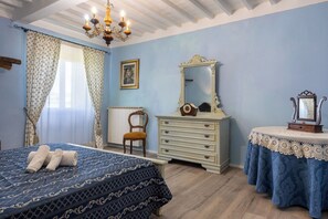 A bedroom with a bed, a dresser, a chair, a table with a lace tablecloth, a mirror, and a chandelier. - Il Cipresso, Casa dei Nonni, Cortona (Cortona)