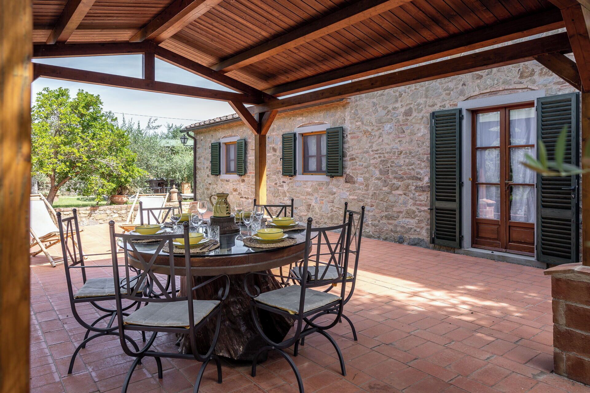 Un espacio de comedor al aire libre con pared de piedra, vigas de madera y una mesa preparada para cuatro.