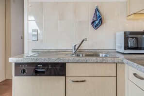 A kitchen with a built-in dishwasher, a stainless steel sink, and a microwave. - Holiday Apartment "Leuchtturm" – Top Floor, Large Balcony & Panoramic Achterwasser View (Mellenthin)