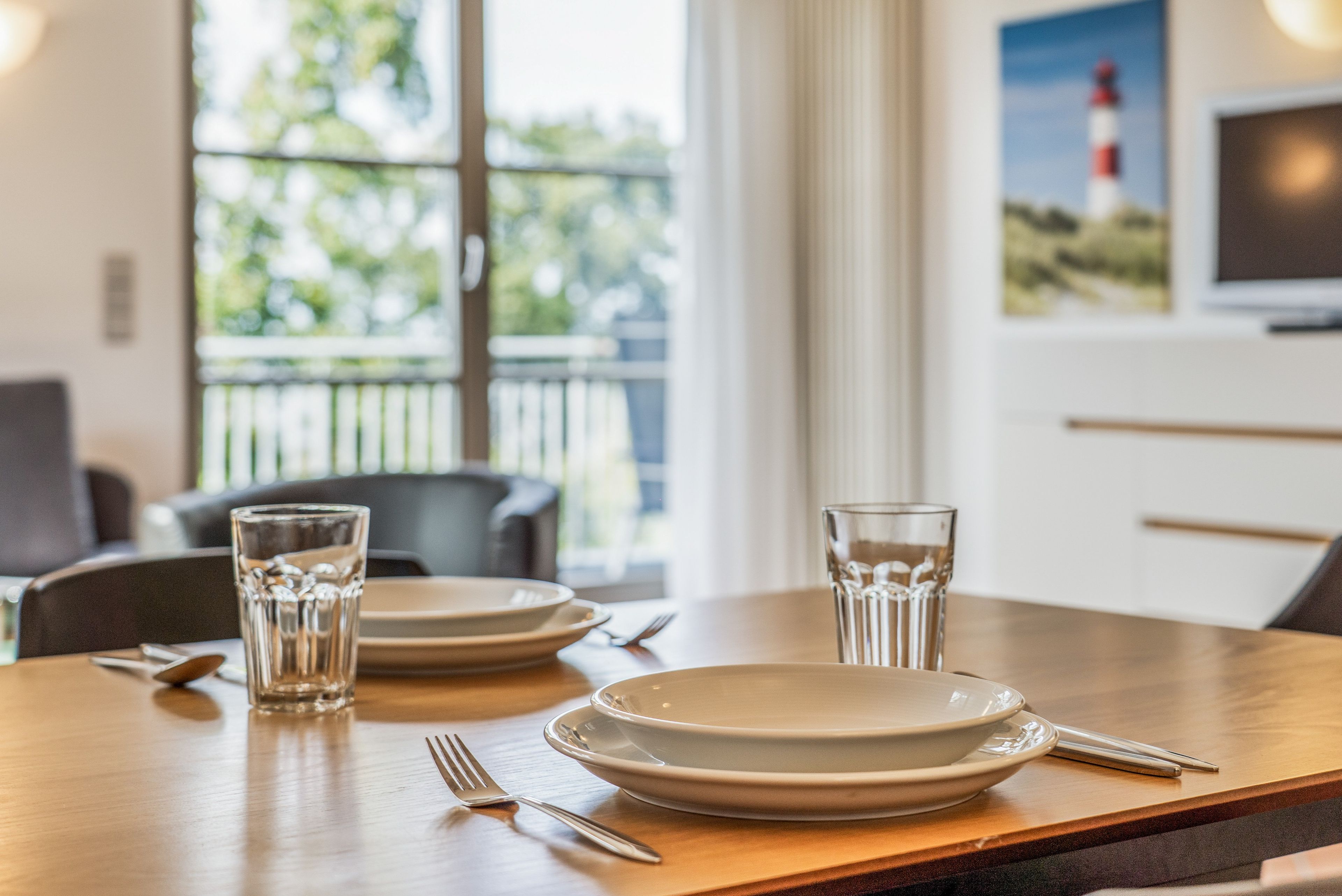 A dining table set with plates, glasses, and cutlery, with a view of greenery and a building outside.