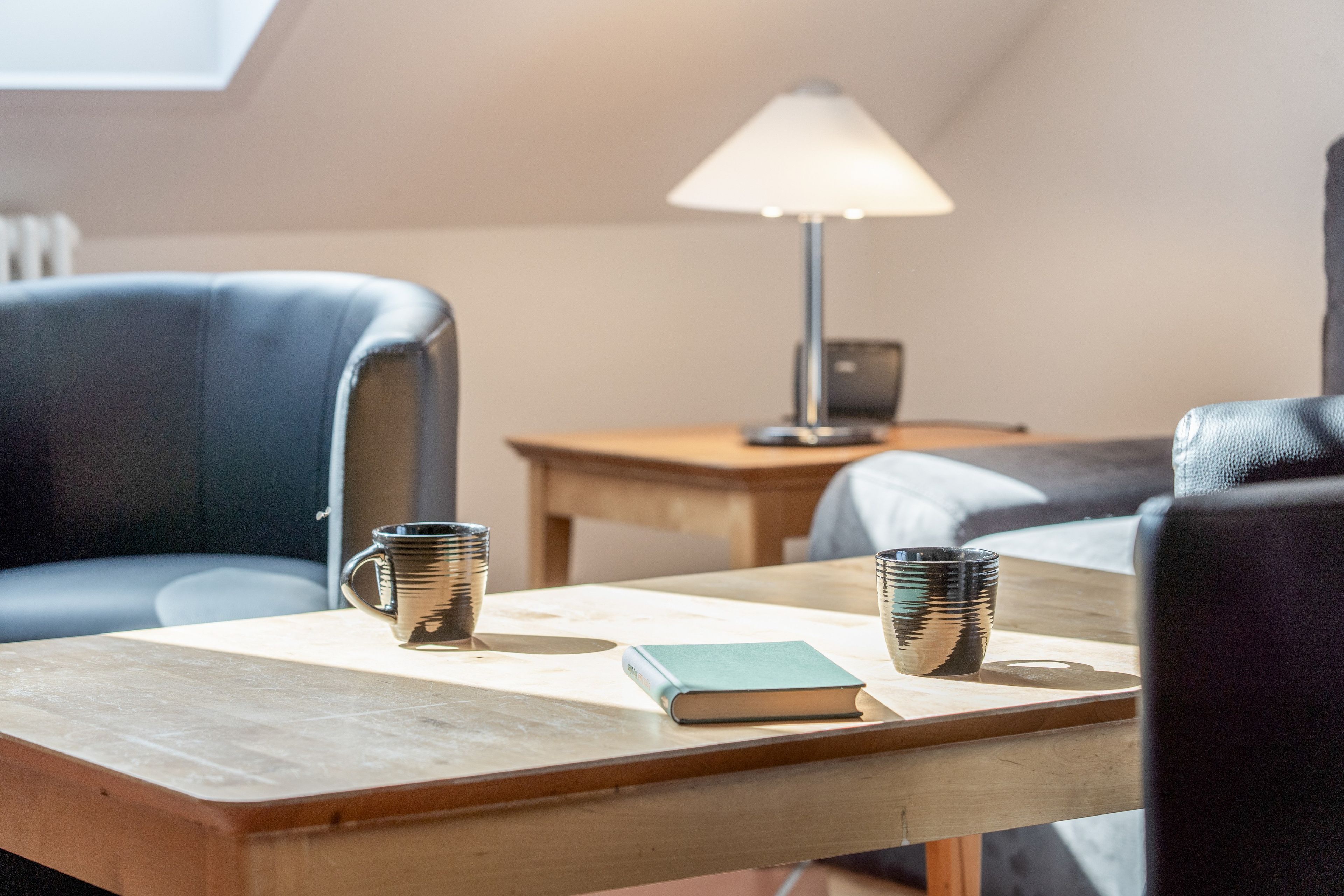 Una habitació amb una taula de fusta, dues cadires, una làmpada, un ordinador portàtil i dues tasses.