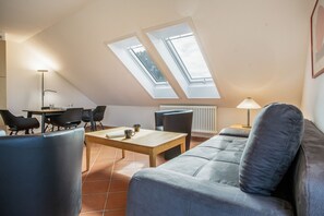A modern loft bedroom with a sloped ceiling, skylights, a sofa, a dining table, and chairs. - Holiday Apartment "Leuchtturm" – Top Floor, Large Balcony & Panoramic Achterwasser View (Mellenthin)