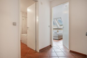 Un couloir mène à une salle de bain avec douche et à une chambre dotée d’une lucarne.